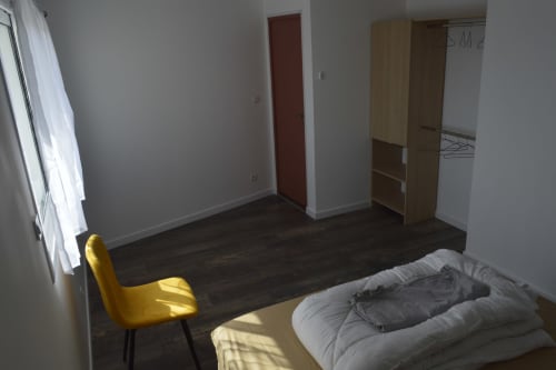 Chambre spacieuse de la Résidence des dunes avec lit, fauteuil jaune, armoire et sol foncé à Landéda
