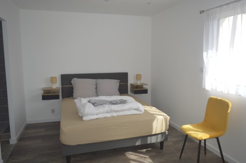 Chambre moderne du gîte Résidence des dunes à Landéda avec lit queen, fauteuil jaune et lumière naturelle de la fenêtre