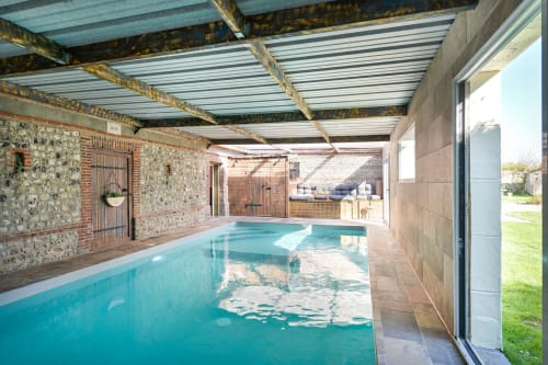 Hallenbad des Hotels Ziane in der Normandie mit türkisblauem Wasser, rustikalen Steinmauern und Holzbalken