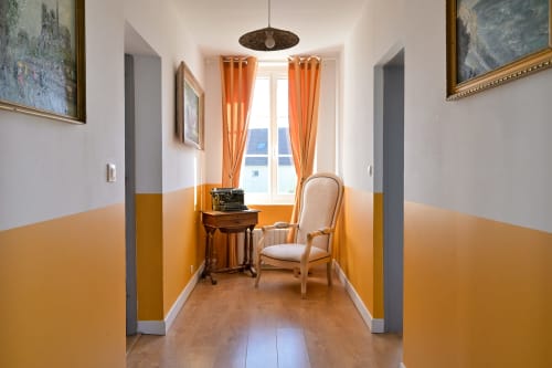 Eleganter Flur des Hotels Ziane in der Normandie mit orangefarbenen Wänden, Holzmöbeln und reichlich natürlichem Licht