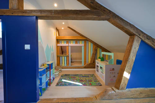 Helles Kinderspielzimmer im Hotel Ziane in der Normandie mit blauen Wänden, Holzbalken, Spielzeug und Spielmatte