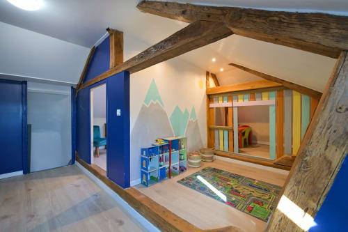 Spielzimmer des Hotels Ziane mit Holzbalken, blauen Wänden, Bergmotiv und farbenfrohem Kinderspielbereich in der Normandie