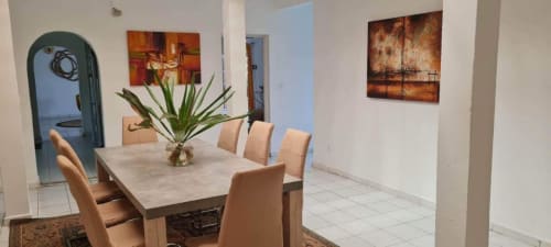 Salle à manger du Kaz Kafe B&B à Mamoudzou avec chaises beiges, table en pierre et art mural contemporain