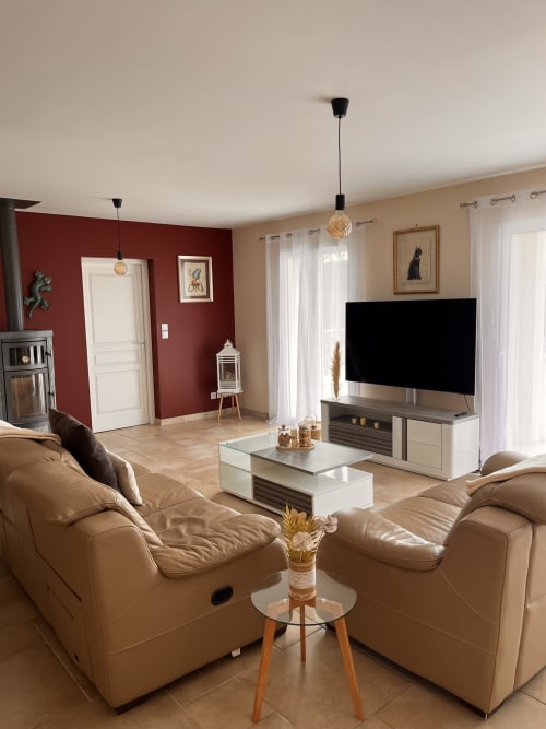Salon de villa moderne avec fauteuils en cuir beige, télévision écran plat, meuble blanc, mur accent rouge et vue sur les montagnes