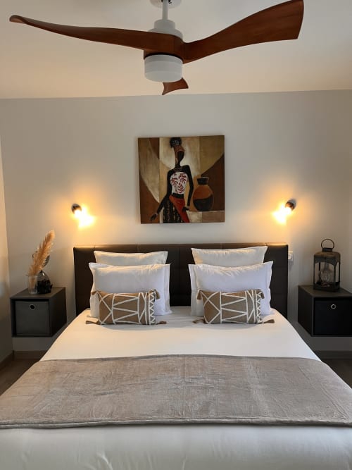 Chambre moderne avec ventilateur de plafond, literie blanche, coussins à motifs, tableaux, appliques murales et tables de nuit, au Gîte la Villa des