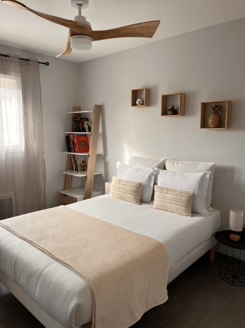 Chambre de la villa moderne avec ventilateur de plafond en bois, lit blanc, accents beige et étagères murales en bois à la Gîte la Villa des Falaises