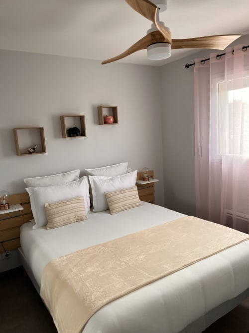 Chambre moderne au Gîte la Villa des Falaises du Lot avec ventilateur de plafond en bois, literie blanche, coussins rayés et applique murale