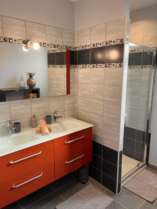 Salle de bain moderne avec vanité rouge, carrelage beige et noir, douche à l'italienne à la Villa des Falaises du Lot en France
