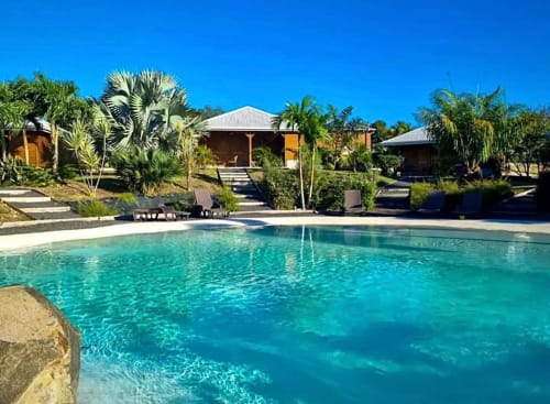 Piscine turquoise aux Cottages du Lagon à Saint-François, Guadeloupe, avec palmiers et bungalows sous un ciel bleu éclatant
