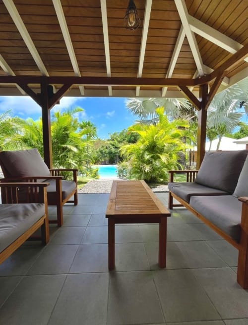 Covered patio with wooden lounge chairs overlooking tropical pool and palm gardens at Cottages du Lagon, Saint-François