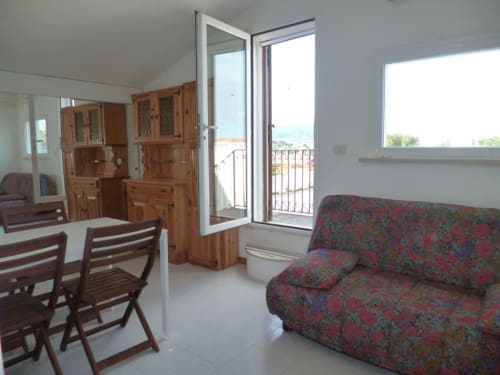 Appartamento Casa Alimento ad Ancona con sala da pranzo arredata, divano rosso a motivi, credenza in legno e accesso al balcone