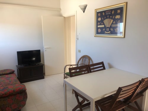 Zona pranzo dell'appartamento di Ancona con tavolo bianco, sedie in legno, TV e carta della pasta italiana sulla parete