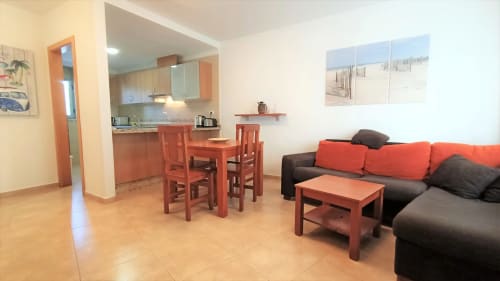 Sala de estar moderna con muebles naranja-rojo, cocina abierta y vistas a la ciudad en El Médano, Canarias