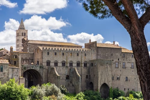 Castello medievale in pietra con campanile presso l'hotel Donkeys & Roses in Italia, circondato da vegetazione verde e cielo azzurro