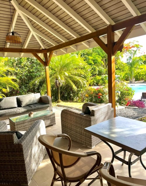 Terrasse couverte du salon des Cottages du Lagon avec mobilier en rotin, vue sur la piscine, jardin tropical et espace repas en plein air