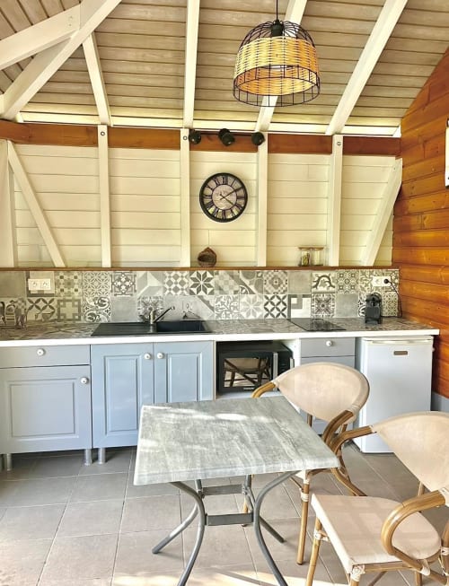 Cuisine extérieure moderne aux Cottages du Lagon avec armoires blanches, dosseret carrelé et coin repas en rotin