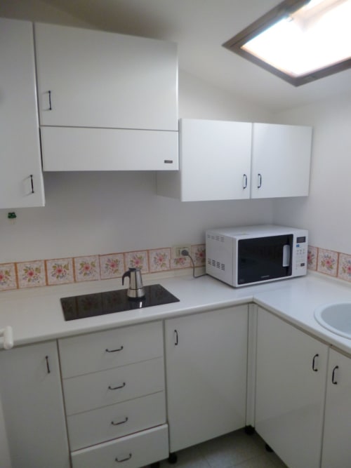 Cucina compatta nell'appartamento di Ancona con mobili bianchi, alzatile con motivi floreali, microonde e lavello