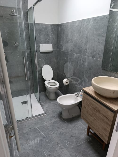 Bagno moderno nell'appartamento Casa Alimento ad Ancona con piastrelle in marmo grigio, doccia, wc, bidet e mobile lavabo in legno