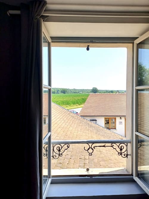 Portes-fenêtres ouvertes du Relais Saint-Laurent révélant la terrasse, le toit et les champs verts de la campagne de Chevreuse
