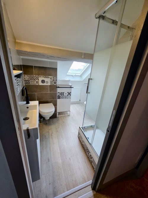 Salle de bain moderne du Relais Saint-Laurent B&B à Chevreuse avec toilettes, lavabo, douche, carrelage à motifs, puits de lumière et bois