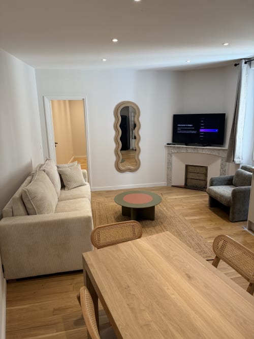 Salon moderne de l'appartement d'Antibes avec canapé crème, cheminée, téléviseur, table à manger en bois et miroir décoratif