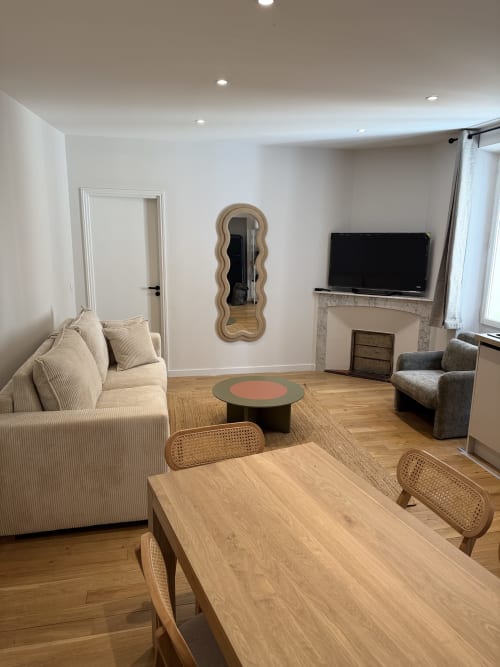 Salon moderne de l'appartement d'Antibes avec canapé crème, table à manger en bois, téléviseur foyer et miroir ondulé