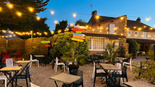 Terrasse extérieure du Relais Saint-Laurent à Chevreuse, France au crépuscule avec guirlandes lumineuses, tables de restaurant et bâtiment en brique