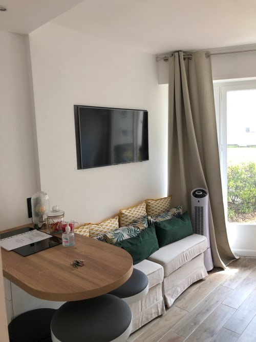 Studio moderne lumineux avec canapé, table en bois, TV murale et vue sur jardin à Angres