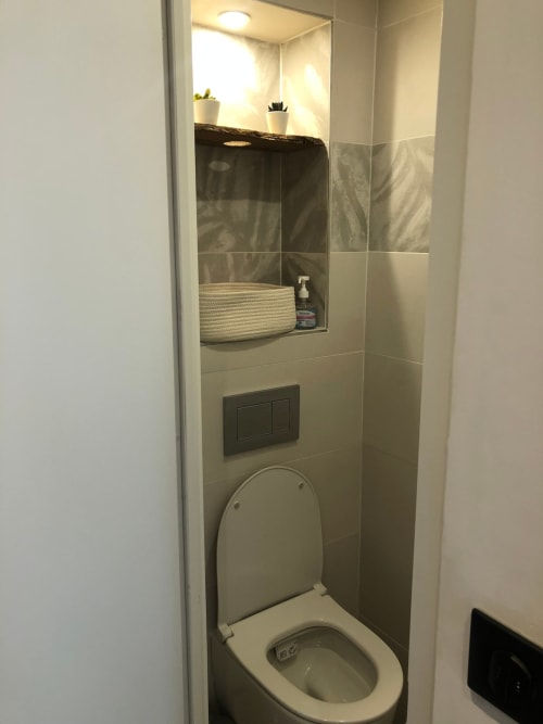 Salle de bain moderne dans l'appartement-hôtel d'Angres avec toilettes, lavabo, miroir, étagère et plantes en pot
