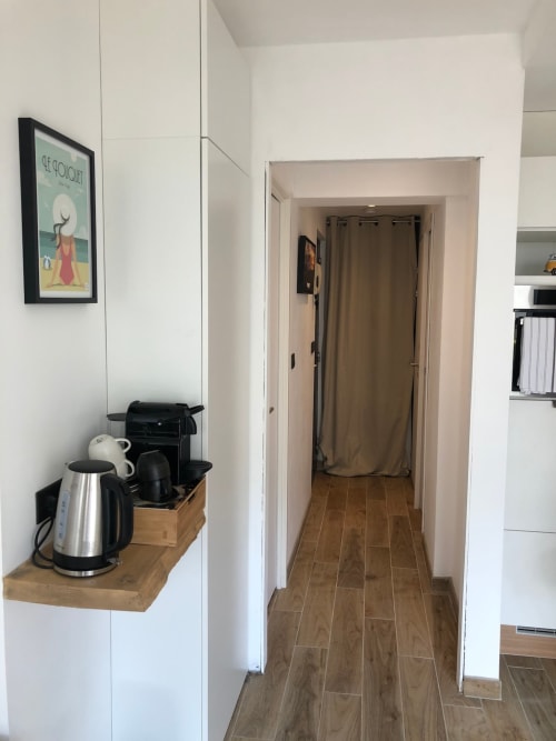 Couloir d'appartement moderne avec parquet, placards blancs, bouilloire électrique et cafetière sur étagère en bois, tons beige