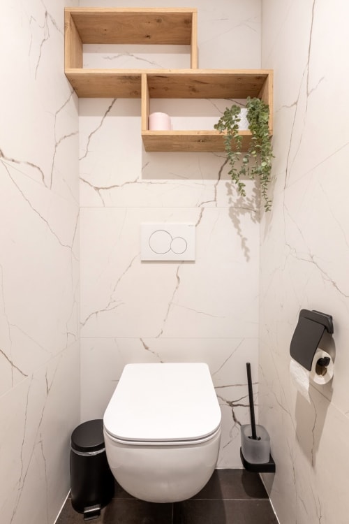 Toilettes modernes avec siège blanc dans l'appartement Le Cocon aux Hébergements C&C, étagères en bois au-dessus avec plante et accessoires