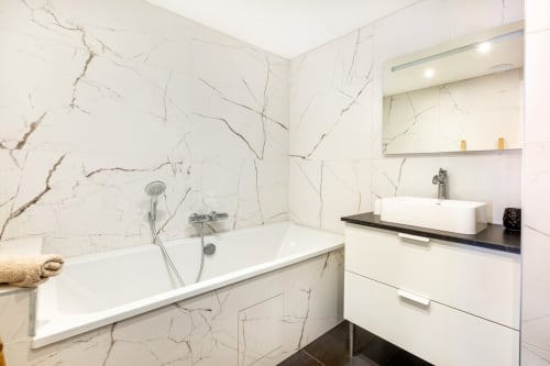 Salle de bain moderne aux murs effet marbre, baignoire blanche, vasque et miroir à l'appartement Le Cocon, Hébergements C&C