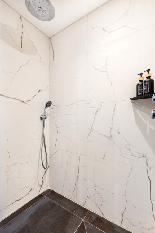 Salle de bain moderne avec parois effet marbre, douchette pluie et articles de toilette à l'appartement Hébergements C&C