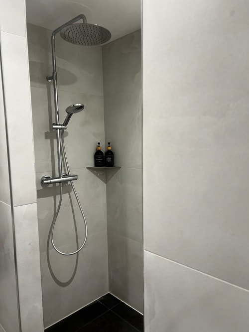 Douche moderne aux Hébergements C&C à Angres avec pomme de douche pluie, douchette à main et flacons noirs sur l'étagère