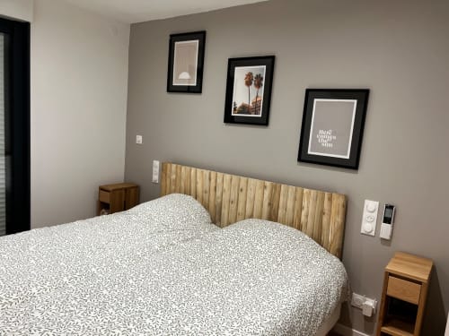 Chambre lumineuse aux Hébergements C&C avec tête de lit en bois, literie à motifs et trois tableaux encadrés sur fond taupe