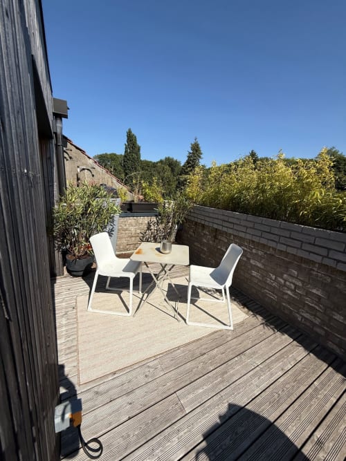 Terrasse sur le toit des Hébergements C&C à Angres avec chaises blanches, table à manger et verdure sous un ciel bleu