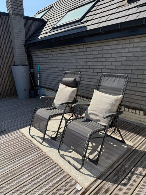Deux chaises longues avec coussins sur la terrasse du toit des Hébergements C&C, Angres, avec bâtiment en brique et puits de lumière.
