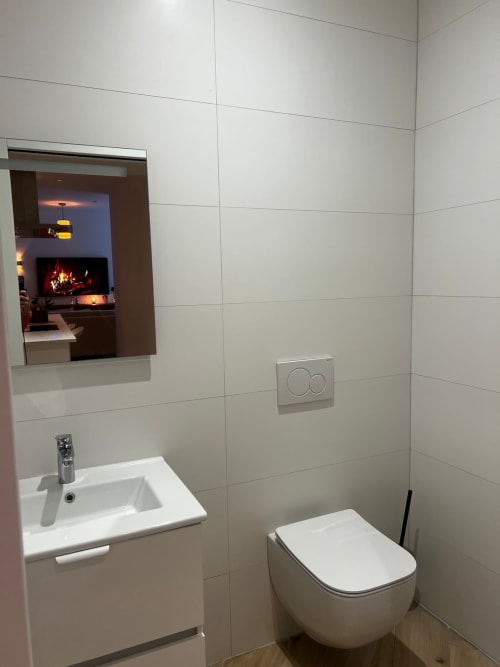 Salle de bain moderne aux Hébergements C&C avec vasque murale, toilettes, miroir et carrelage à Angres.