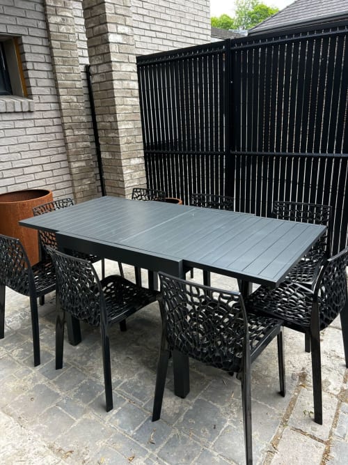 Espace de repas extérieur moderne aux Hébergements C&C à Angres avec table et chaises noires sur terrasse, à côté d'un bâtiment en brique