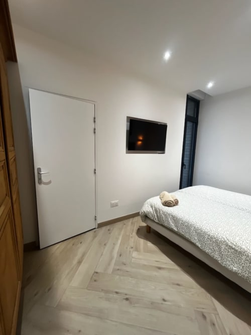 Chambre moderne aux Hébergements C&C à Angres avec lit simple, TV murale, porte blanche et sol en bois clair
