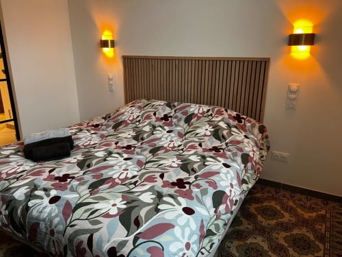 Chambre moderne avec literie à motifs floraux, éclairage mural et tête de lit rembourrée aux Hébergements C&C à Angres.