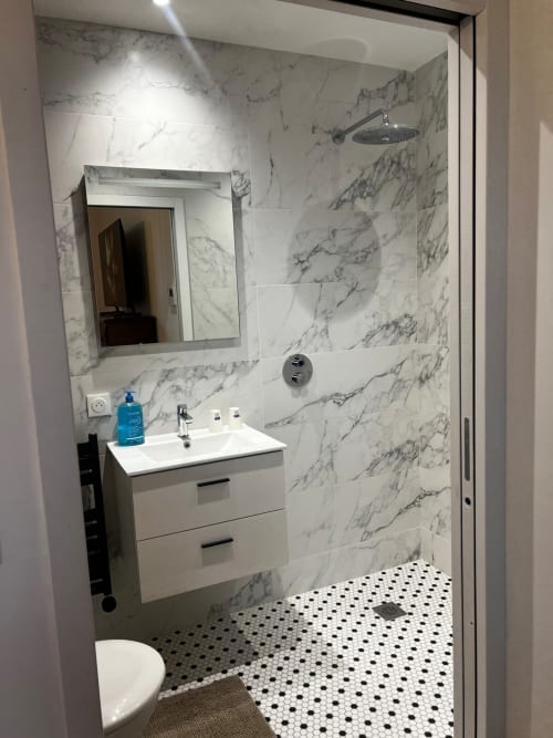 Salle de bain moderne aux Hébergements C&C avec carrelage imitation marbre, vasque blanche, pommeau de douche cascade et mosaïque noir et blanc