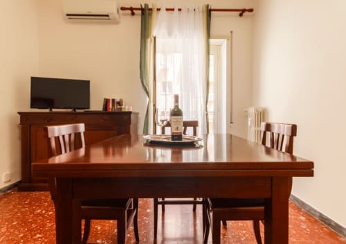 Spaziosa sala da pranzo della Roma Magic Flat con tavolo in legno, sedie, TV, bottiglia di vino e arredi eleganti con vista