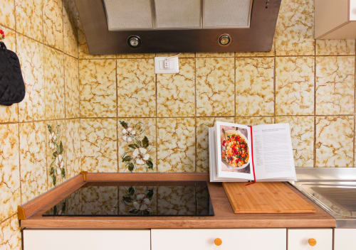 Bancone della cucina di Roma Magic Flat con backsplash in marmo color crema, piano cottura e ricettario aperto a una ricetta colorata