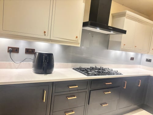 Modern kitchen with cream and charcoal cabinetry, white countertop, black range hood, gas cooktop, and air fryer at England