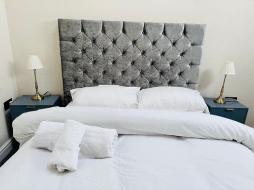 Modern bedroom with gray quilted headboard, white bedding, and side tables with brass lamps at England Furnished Homes in