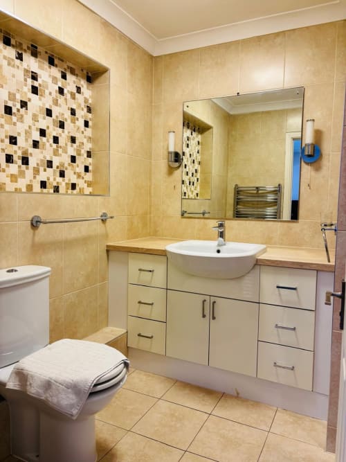 Modern bathroom with beige tile walls, white vessel sink, vanity storage, toilet, and decorative mosaic tile accents in