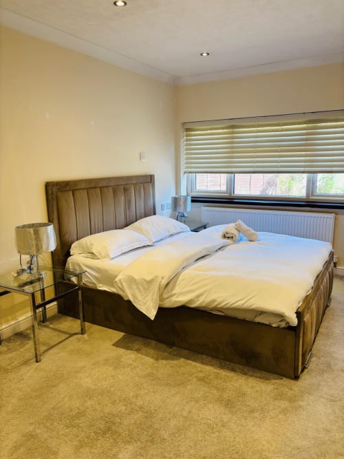 Spacious furnished bedroom in High Wycombe with brown upholstered bed, yellow walls, garden view windows, and modern