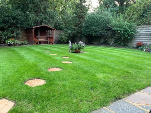 Spacious garden with stepping stone pathway, wooden arbor, flowering plants, and manicured lawn at Egham furnished home in