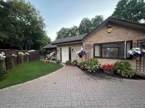 Brick bungalow with paved driveway, colorful flower beds, and manicured garden in High Wycombe, England
